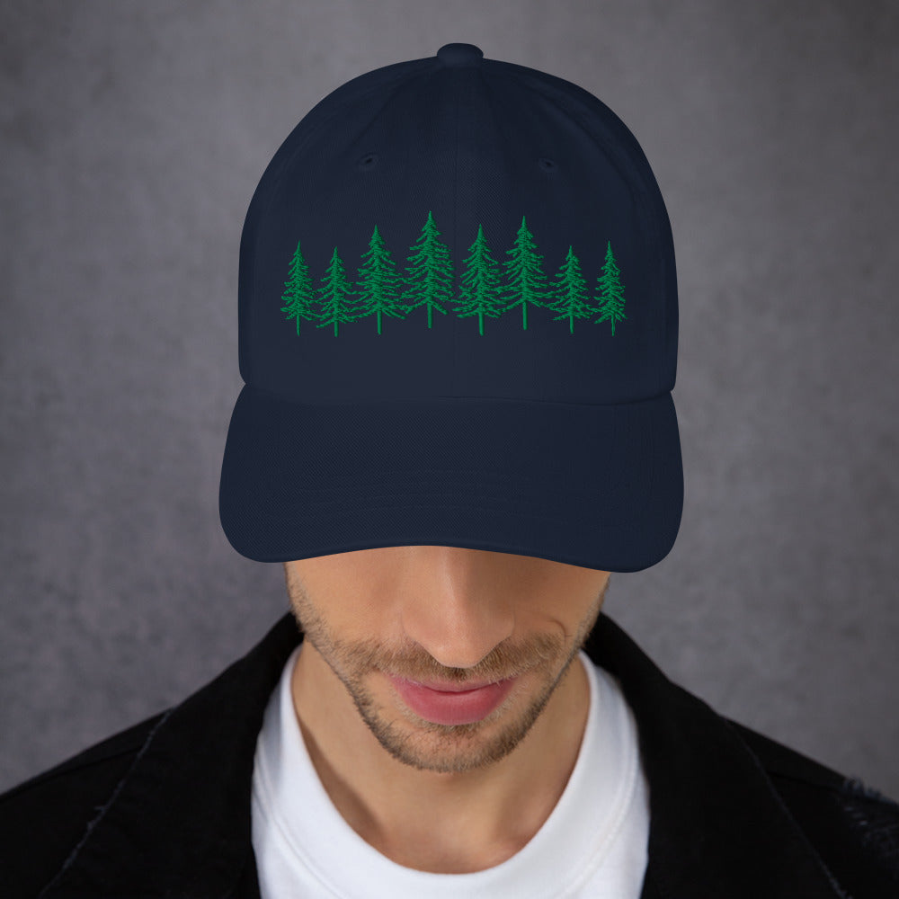 Male model wearing the navy Into the Pines baseball hat by Klemm & Co., front view showing the embroidered pine tree design in green thread.