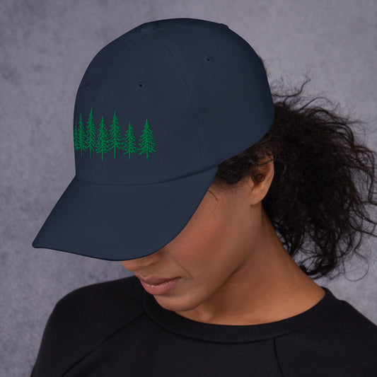 Female model wearing the navy Into the Pines baseball hat by Klemm & Co., front-left view showing the embroidered pine tree design in green thread.