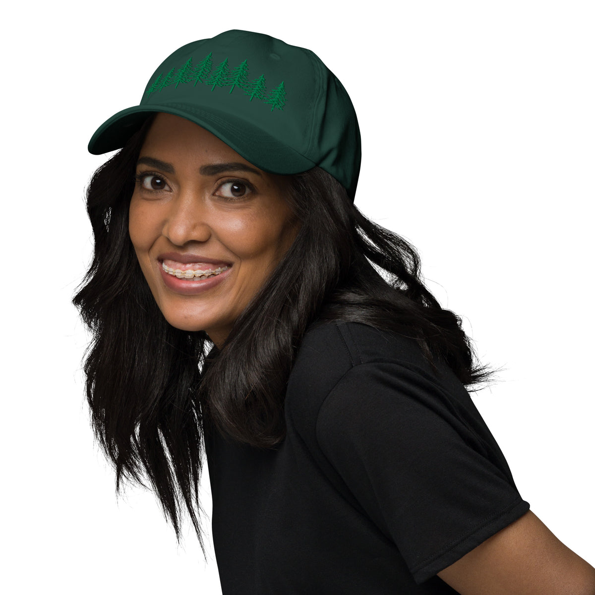 Female model wearing the green Into the Pines baseball hat by Klemm & Co., angled left to show the pine tree design embroidered in green thread.