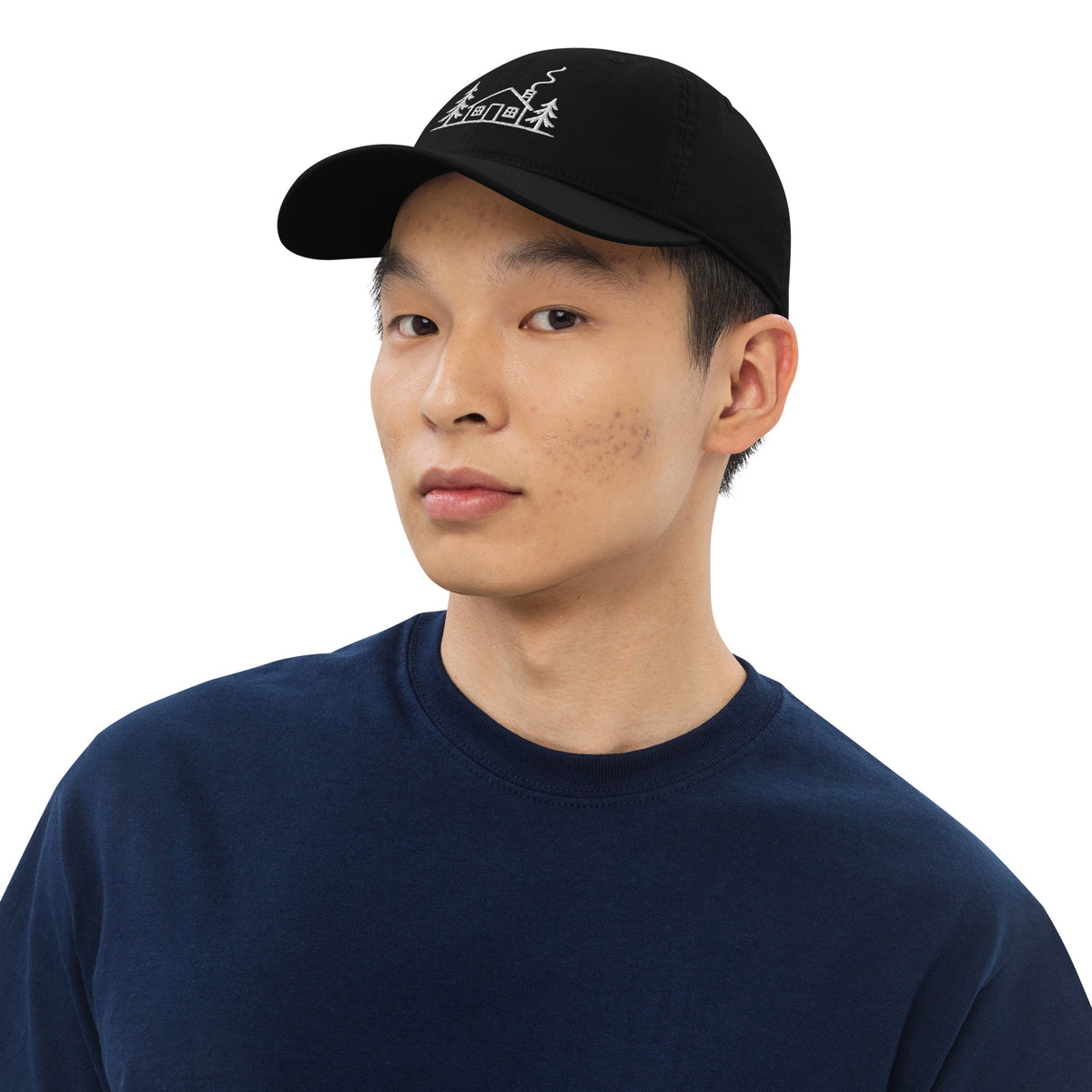 Male model wearing the black Meet Me at the Cabin baseball hat by Klemm & Co., featuring the white embroidered cabin and pine tree design.