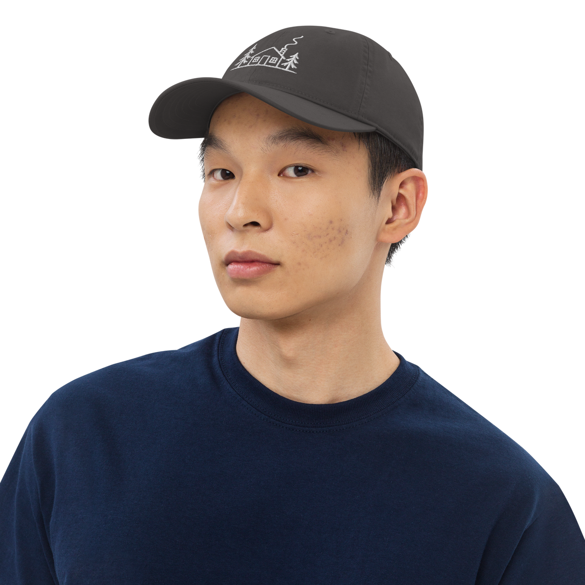 Male model wearing the grey Meet Me at the Cabin baseball hat by Klemm & Co., featuring the white embroidered cabin and pine tree design.