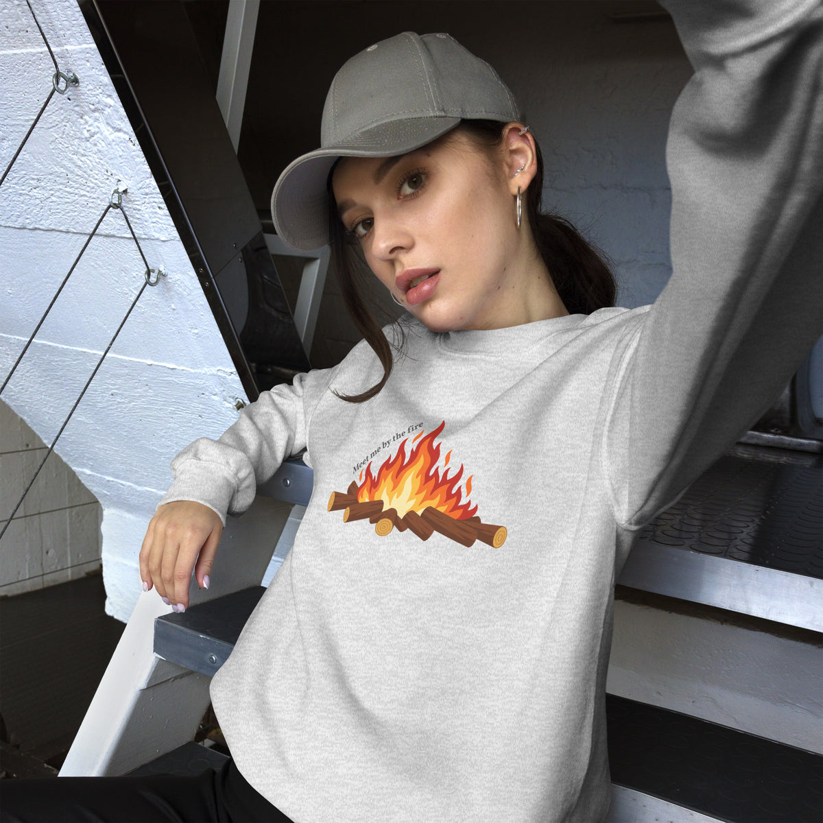 Female model wearing the ash Meet Me by the Fire crewneck sweatshirt by Klemm & Co., front view with one arm raised, showing the printed campfire design.