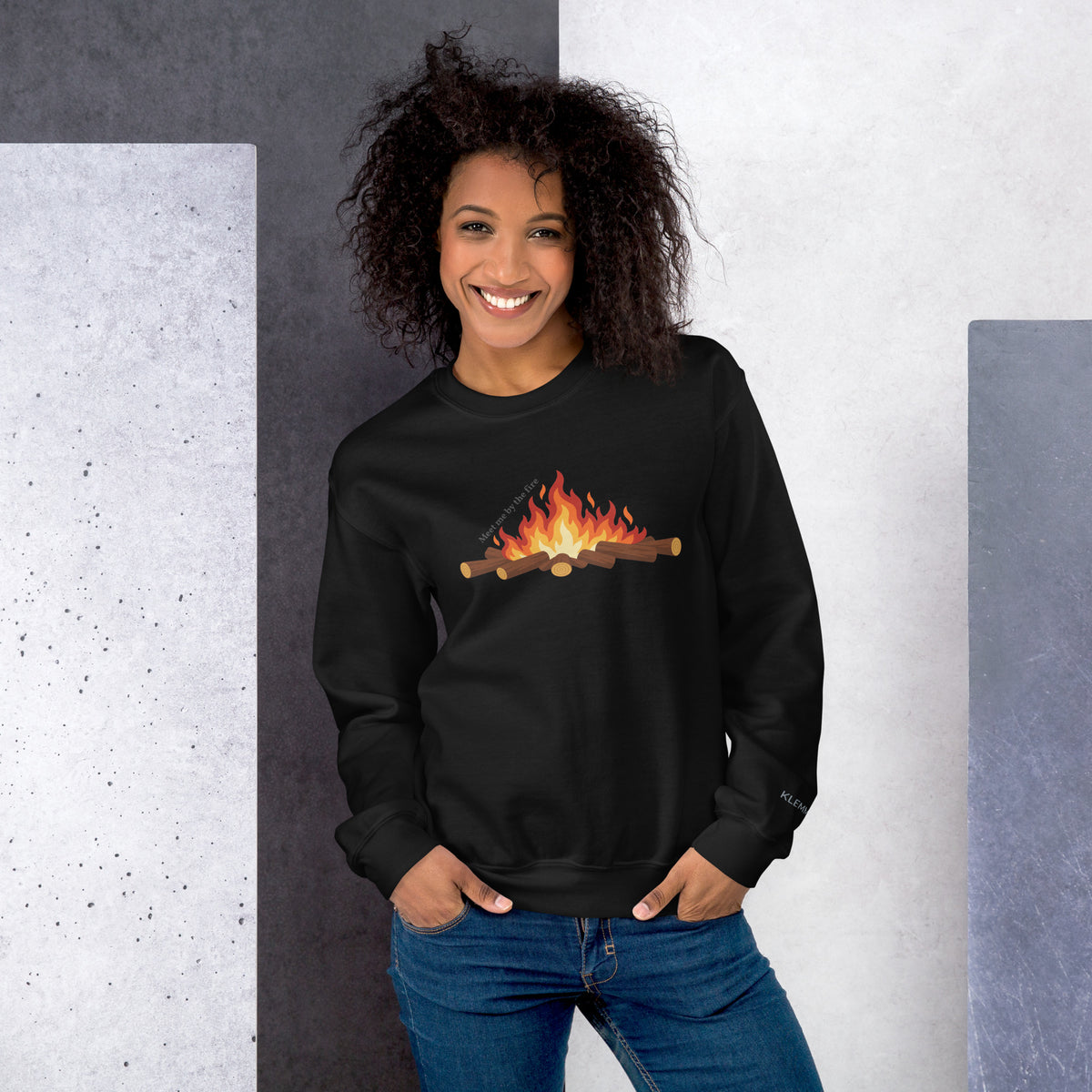 Female model wearing the black Meet Me by the Fire crewneck sweatshirt by Klemm & Co., front view showing the printed campfire design.