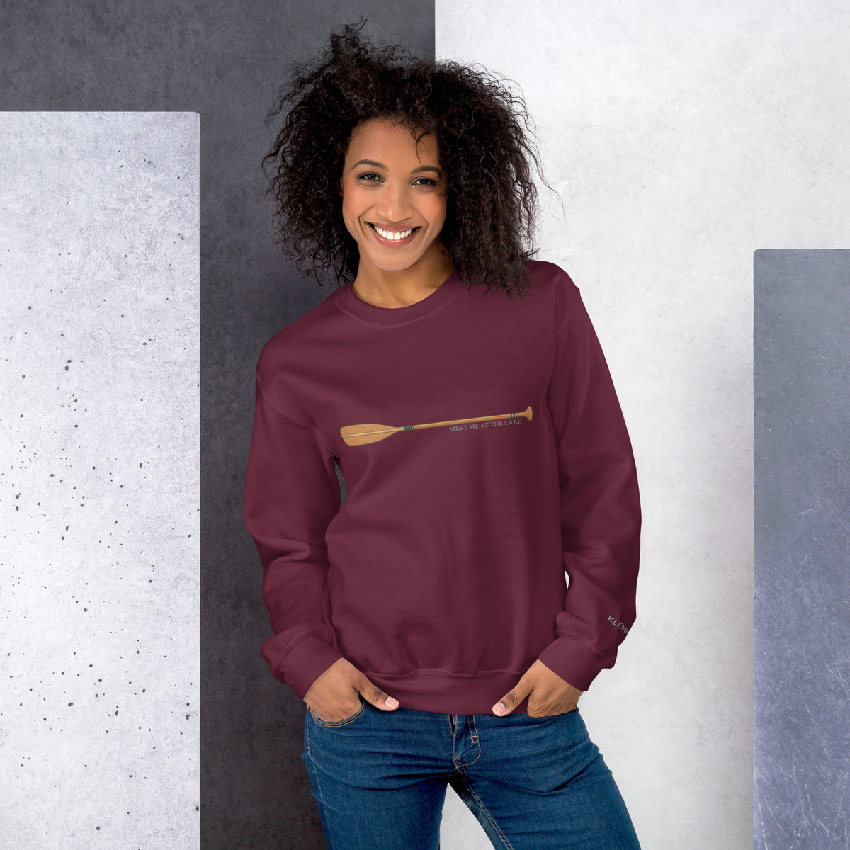 Female model wearing the maroon Meet Me at the Lake crewneck sweatshirt by Klemm & Co., front view showing the printed paddle design.