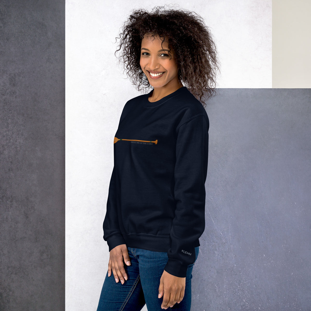 Female model wearing the navy Meet Me at the Lake crewneck sweatshirt by Klemm & Co., front-left view showing the printed paddle design and KLEMM sleeve branding.