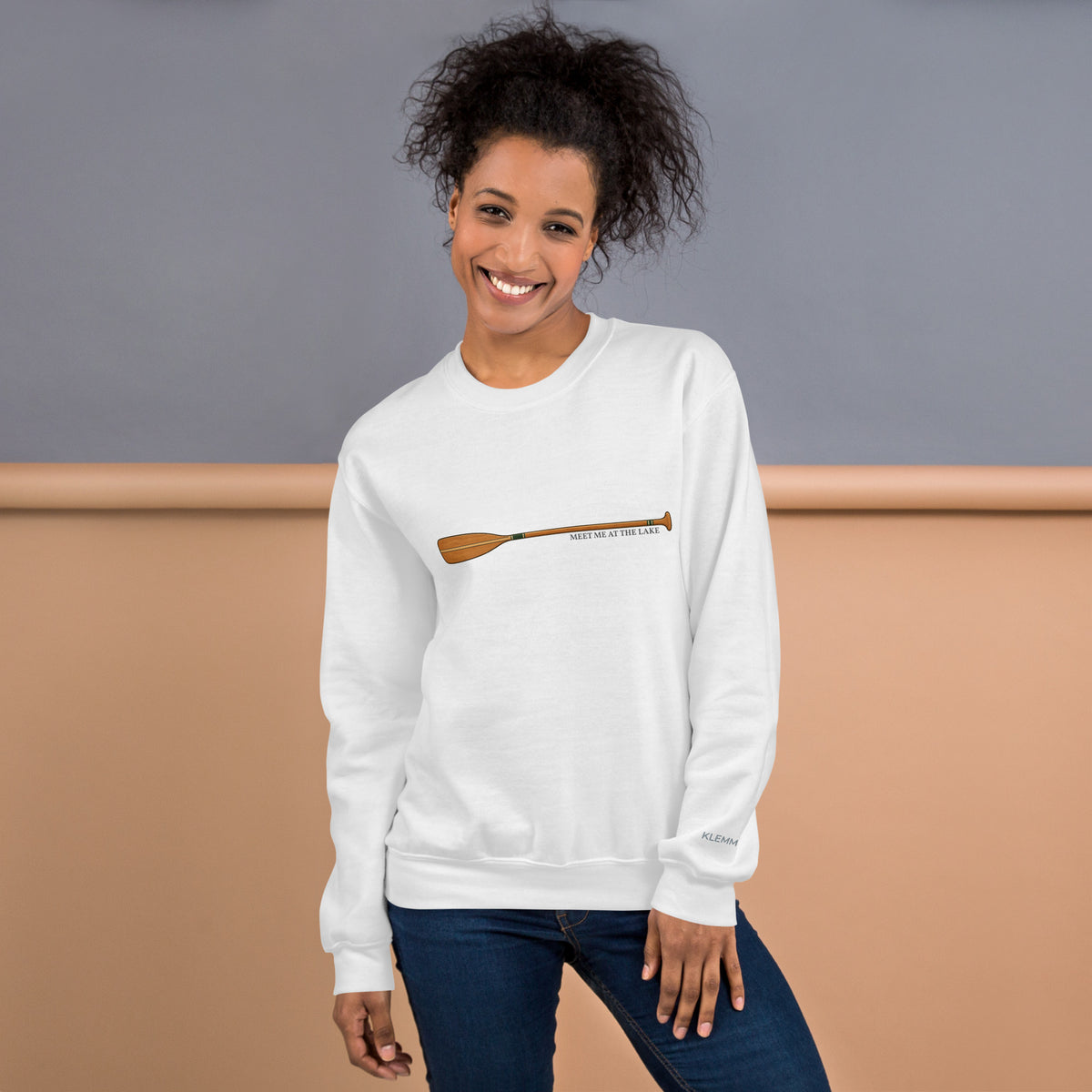 Female model wearing the white Meet Me at the Lake crewneck sweatshirt by Klemm & Co., front view showing the printed paddle design.