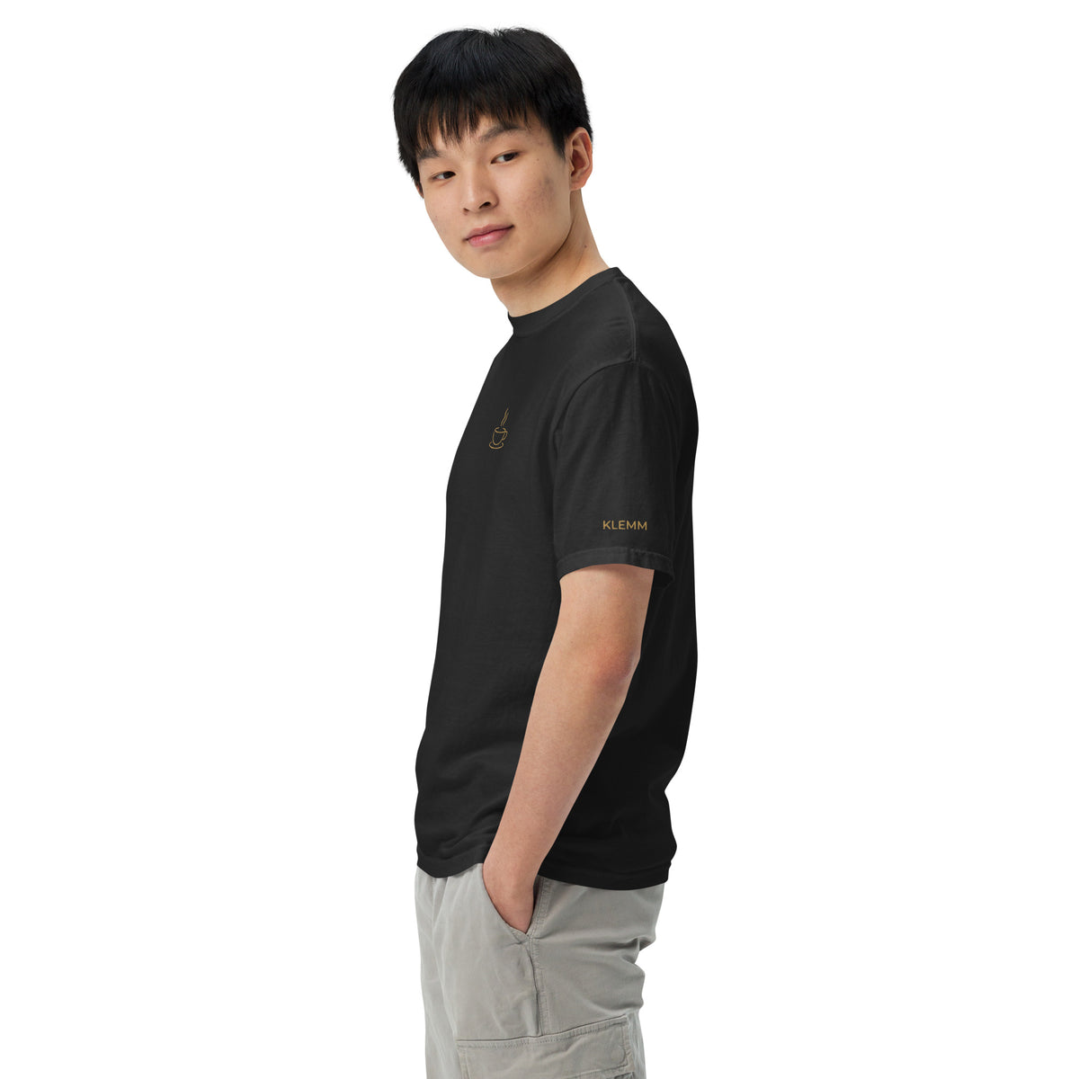 Male model wearing the black Poured for This coffee T-shirt by Klemm & Co., left side view showing KLEMM embroidered in gold thread on the sleeve.