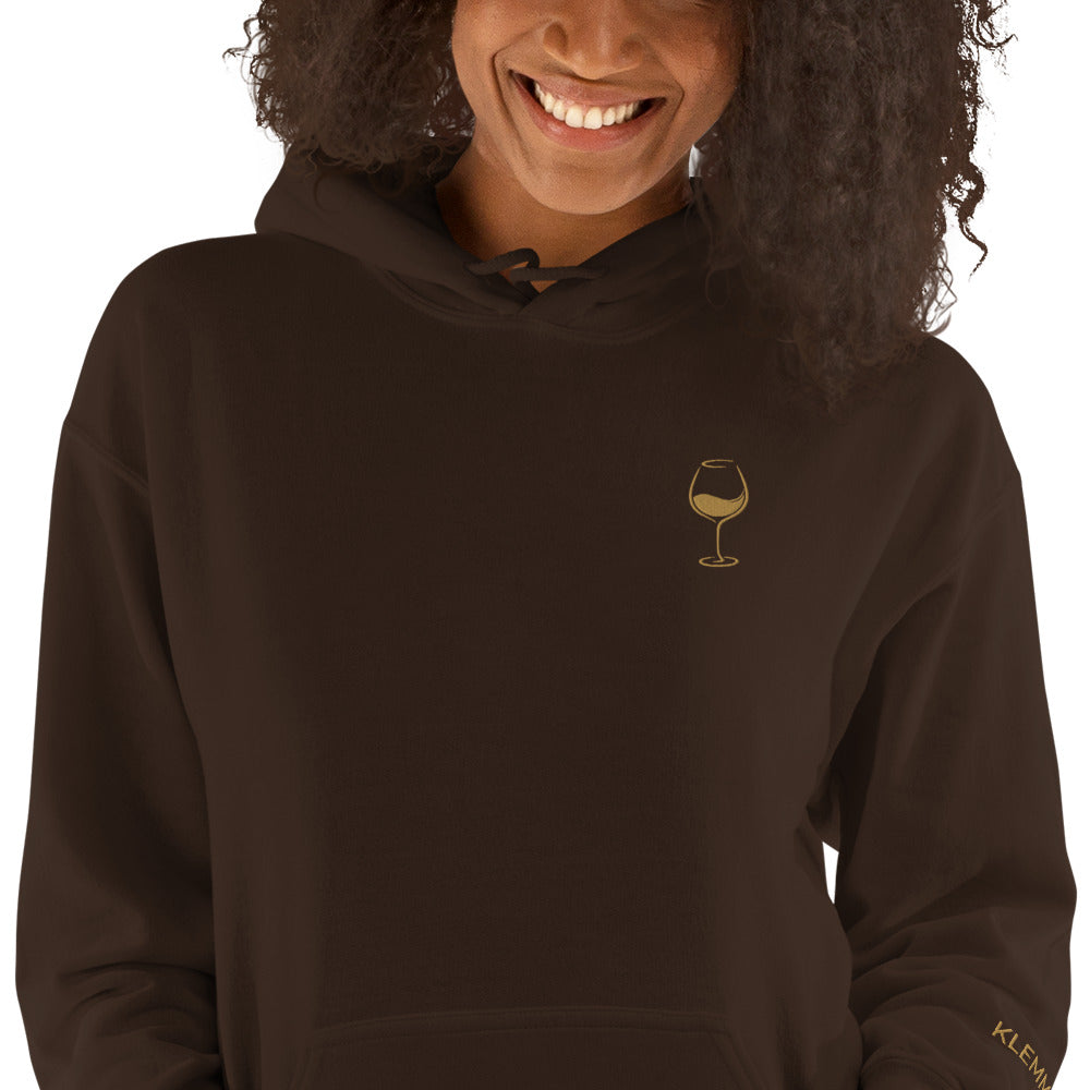 Female model wearing the dark chocolate Poured for This wine hoodie by Klemm & Co., cropped from the smile down to show the gold embroidered wine glass on the front.