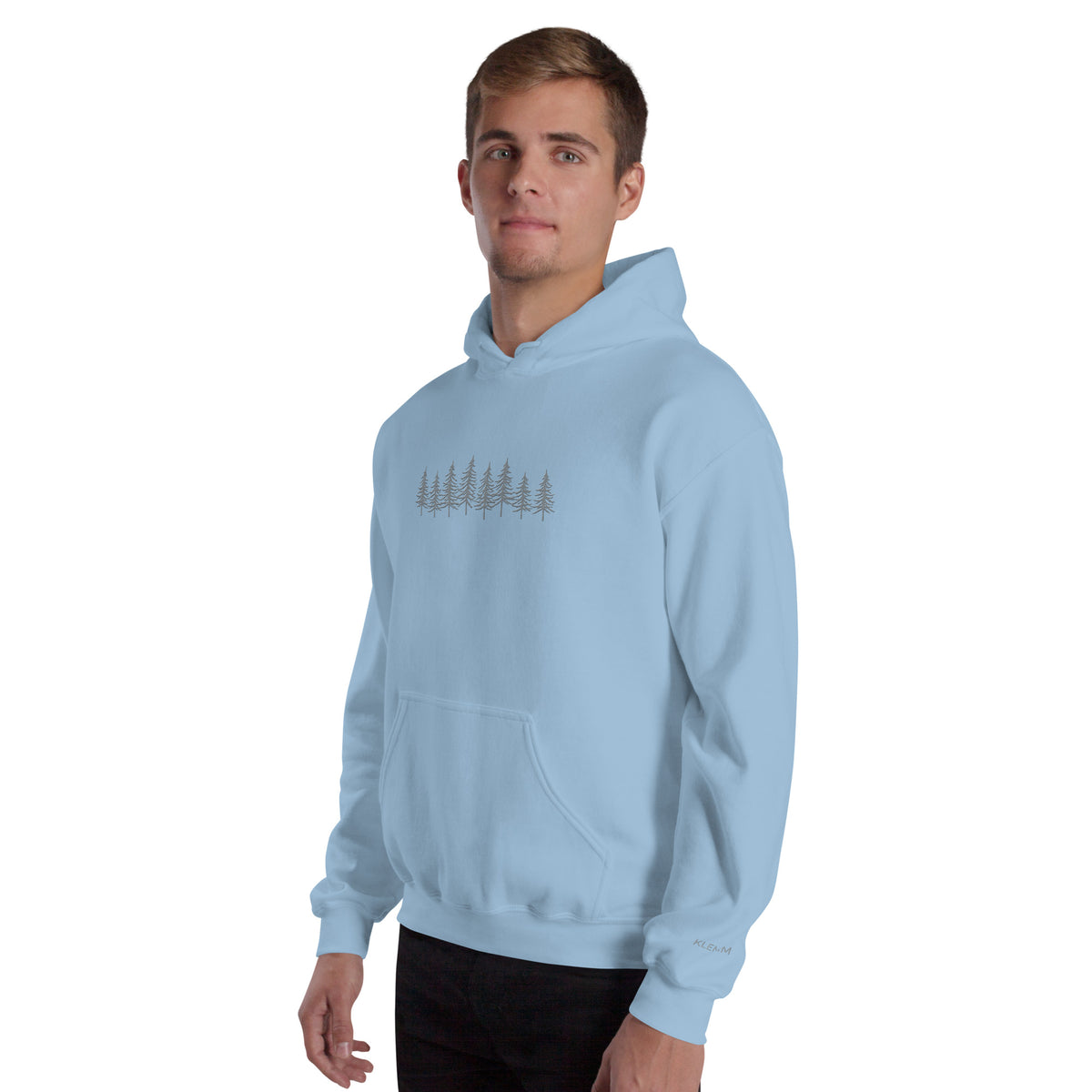 Male model wearing the light blue Into the Pines embroidered hoodie by Klemm & Co., front-left view showing the grey embroidered pine tree design and KLEMM sleeve branding.