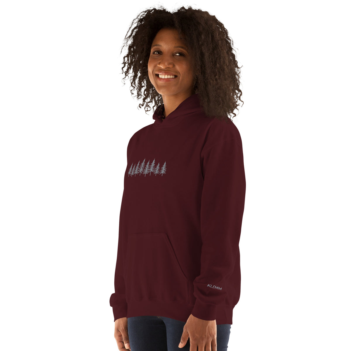 Female model wearing the maroon Into the Pines embroidered hoodie by Klemm & Co., front-left view showing the grey embroidered pine tree design and KLEMM sleeve branding.
