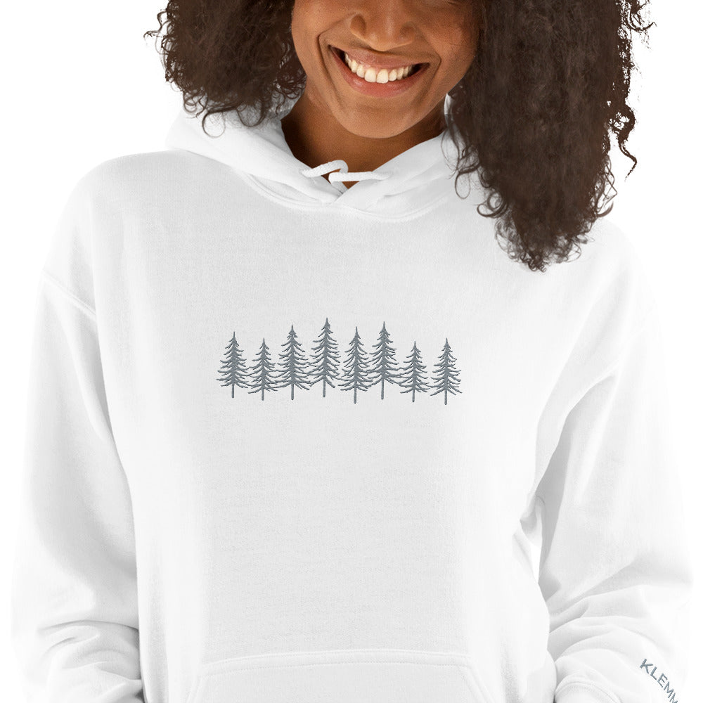 Close-up of a female model wearing the white Into the Pines embroidered hoodie by Klemm & Co., showing the pine tree design embroidered in grey thread.