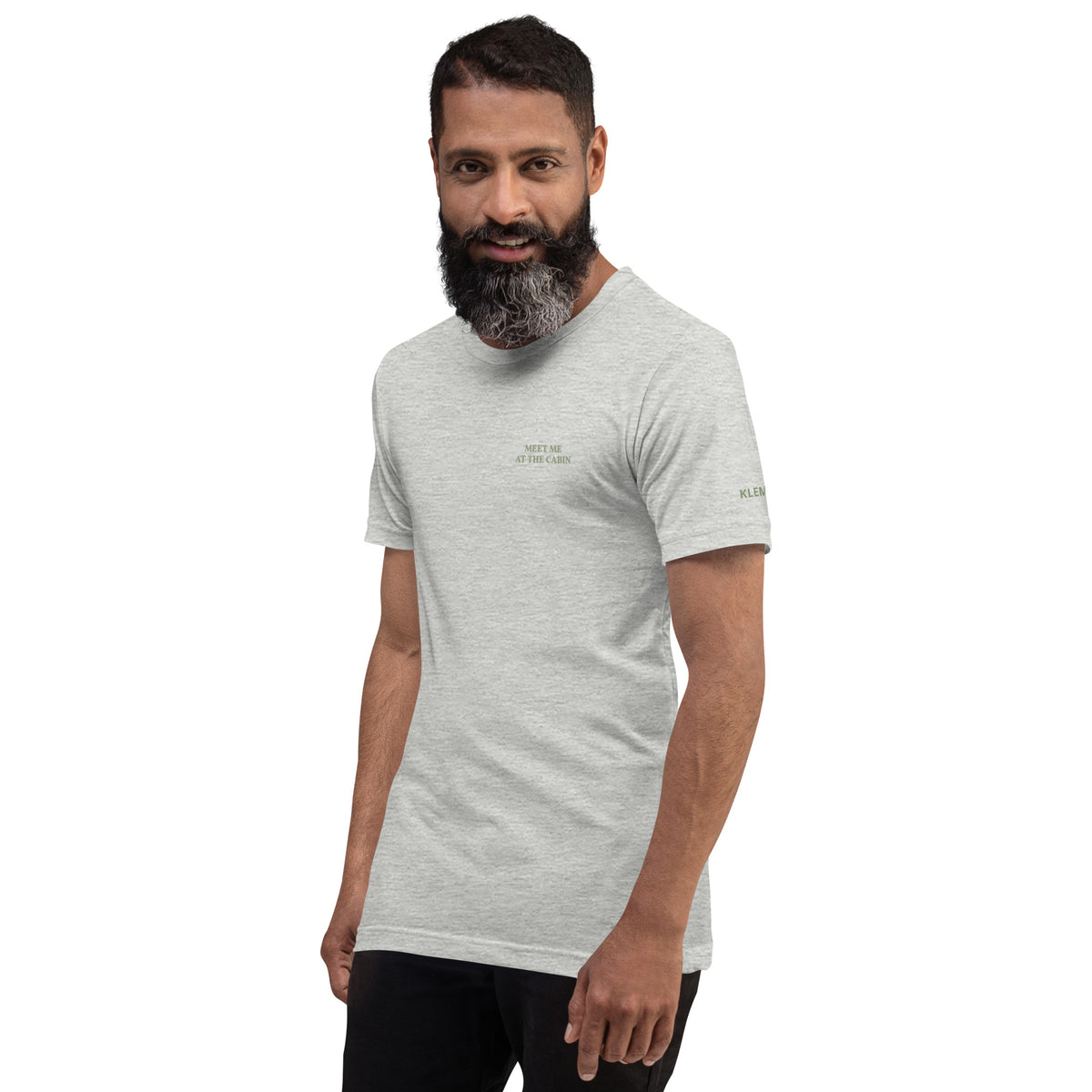 Model wearing the light grey Meet Me at the Cabin graphic T-shirt by Klemm & Co., front view showing the subtle green chest text.