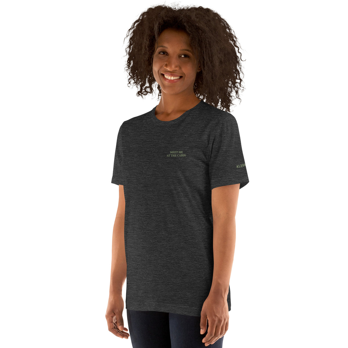 Model wearing the dark grey Meet Me at the Cabin graphic T-shirt by Klemm & Co., showing the subtle green chest text.