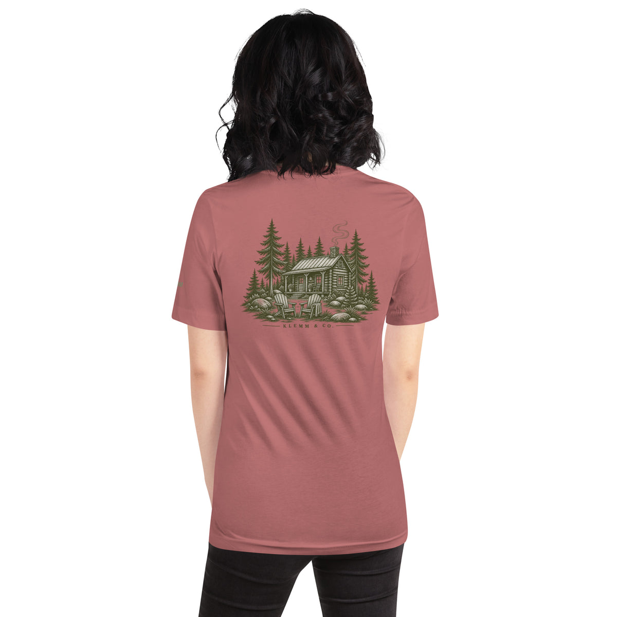 Model wearing the mauve Meet Me at the Cabin graphic T-shirt by Klemm & Co., showing the woodland cabin and pine tree back design.